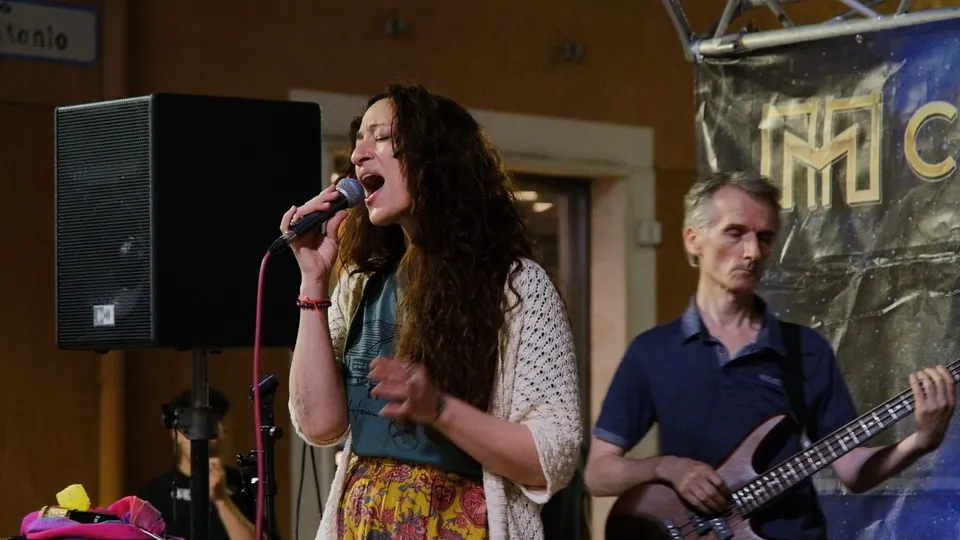 Serena Scocca canta al microfono, dietro di lei Antonio Lanni al basso durante un concerto in piazza